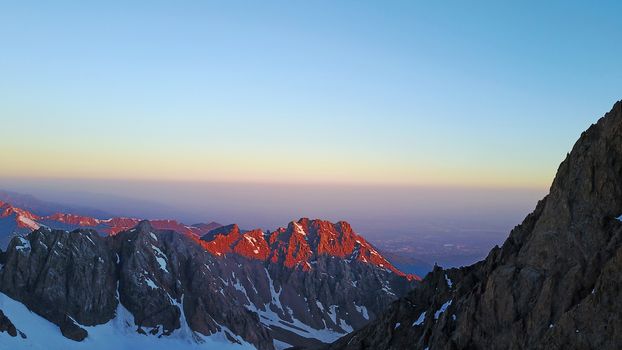 Epic red dawn on top of snowy mountains. Top view from a drone. Huge rocks covered with snow, the ledge of snow overhangs. An avalanche-prone place. Climb to the peak. Flying above the peak. Almaty