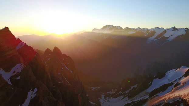 Epic red dawn on top of snowy mountains. Top view from a drone. Huge rocks covered with snow, the ledge of snow overhangs. An avalanche-prone place. Climb to the peak. Flying above the peak. Almaty