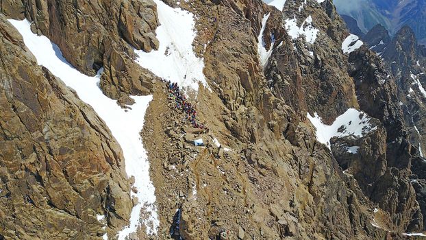 Huge snow mountains. View from the top of the drone. In places, you can see small people climbing to the top. Panorama of steep peaks and rocks, snow cornices. Mountaineering class. Extreme rest.