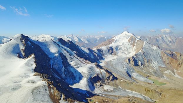 Huge snow mountains. View from the top of the drone. In places, you can see small people climbing to the top. Panorama of steep peaks and rocks, snow cornices. Mountaineering class. Extreme rest.