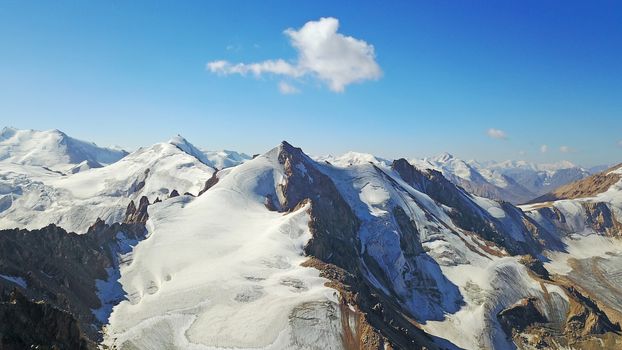 Huge snow mountains. View from the top of the drone. In places, you can see small people climbing to the top. Panorama of steep peaks and rocks, snow cornices. Mountaineering class. Extreme rest.