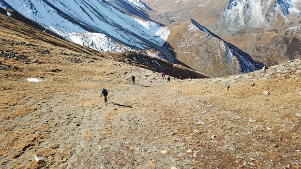 A group of tourists stands on the mountainside. There is snow in places. Very large stones on the sides. Blue sky with white clouds. Top view from the throne. Mountainous area of Kazakhstan.