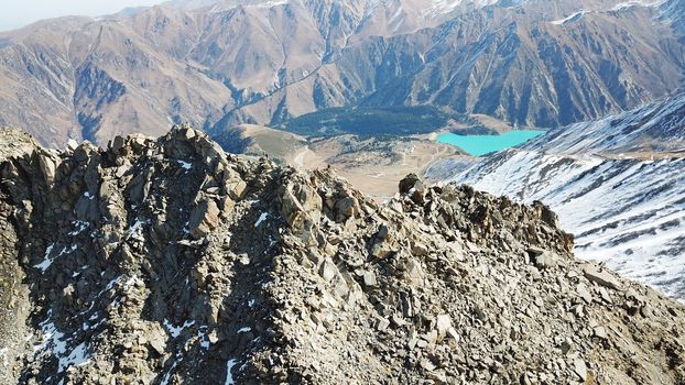 Top view of a group of tourists on top of a snowy peak. Huge rocks covered with snow. Climbers take photos from the top, pose. Flying above the mountains. Blue sky and steep slopes. Kazakhstan.