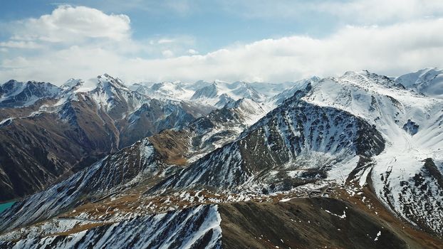 Mountain tops covered with snow. View from a drone. Huge rocks lie on the steep slopes of the mountains. Snow-capped peaks can be seen in the distance, sometimes flashing the city in the smog.