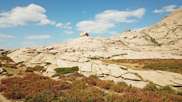 Huge rocks from lava. A former volcano. Bektau-ATA Tract. Large rocks, rifts, cracks, and mountains. In places, grass grows and water is visible. Unusual Martian landscape. Blue sky and clouds.