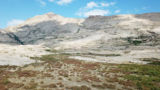 Huge rocks from lava. A former volcano. Bektau-ATA Tract. Large rocks, rifts, cracks, and mountains. In places, grass grows and water is visible. Unusual Martian landscape. Blue sky and clouds.