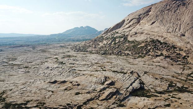 Huge rocks from lava. A former volcano. Bektau-ATA Tract. Large rocks, rifts, cracks, and mountains. In places, grass grows and water is visible. Unusual Martian landscape. Blue sky and clouds.