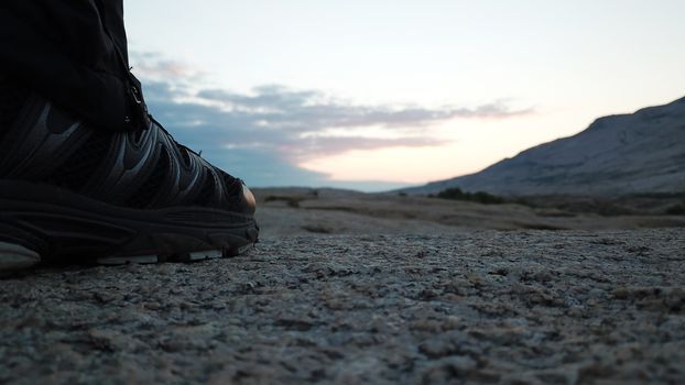 Men's feet in sneakers in the mountains. I walked through the frozen lava in the Bektau-ATA mountains. Dawn over the mountains. In the distance, you can see clouds and Golden rays of the sun.