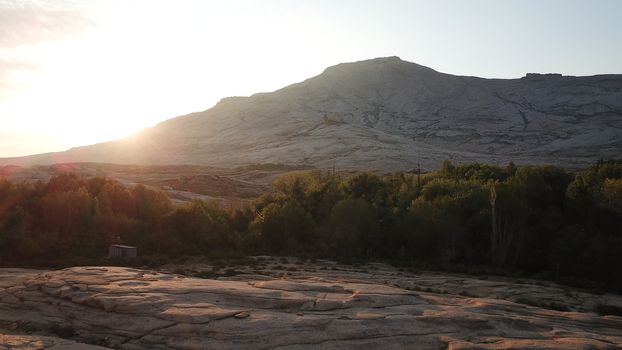 Dawn over frozen lava and mountains. Huge rocks and a gorge cast a shadow from the sun. Grass and trees grow in places. Houses are visible. Clouds in sky and bright rays of the sun. Beautiful gorge.