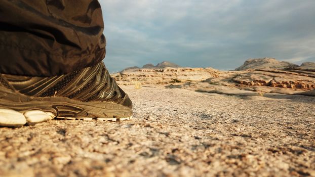 Men's feet in sneakers in the mountains. I walked through the frozen lava in the Bektau-ATA mountains. Dawn over the mountains. In the distance, you can see clouds and Golden rays of the sun.