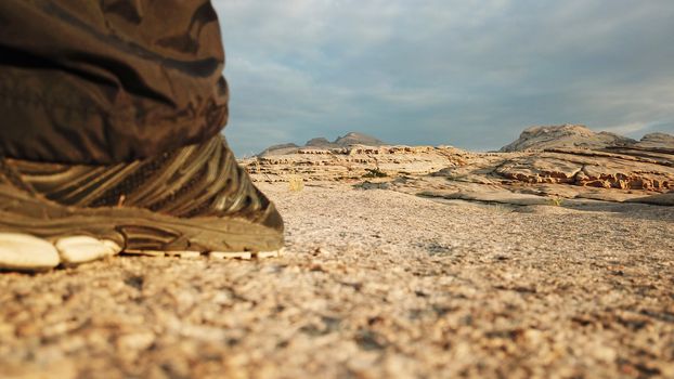 Men's feet in sneakers in the mountains. I walked through the frozen lava in the Bektau-ATA mountains. Dawn over the mountains. In the distance, you can see clouds and Golden rays of the sun.