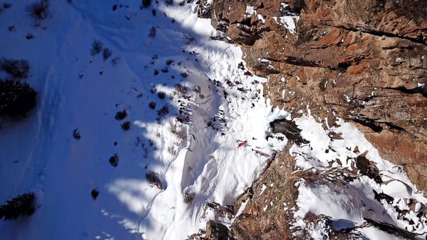 Freezing waterfall in the snowy mountains. View from the drone, from above. The rocks are covered with snow and ice. A small stream of water runs. The waterfall freezes. A group of people are resting