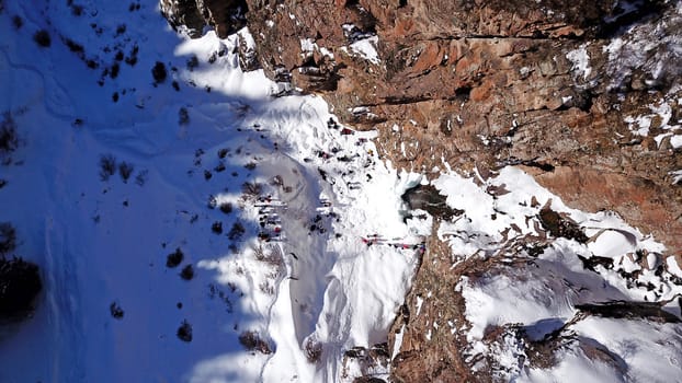 Freezing waterfall in the snowy mountains. View from the drone, from above. The rocks are covered with snow and ice. A small stream of water runs. The waterfall freezes. A group of people are resting