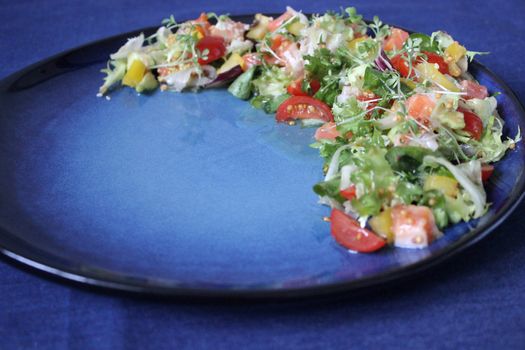 Fresh salad with tomatoes and herbs on a blue plate.Health food.