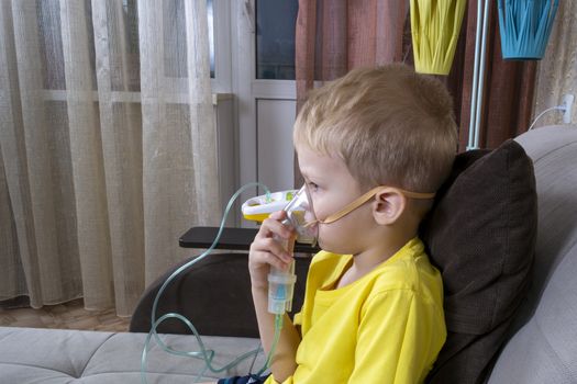 a 5-7 year old boy in a t-shirt takes an inhalation at home