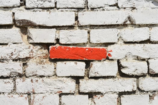 Detail of an old brick wall painted in white with one red brick in the middle