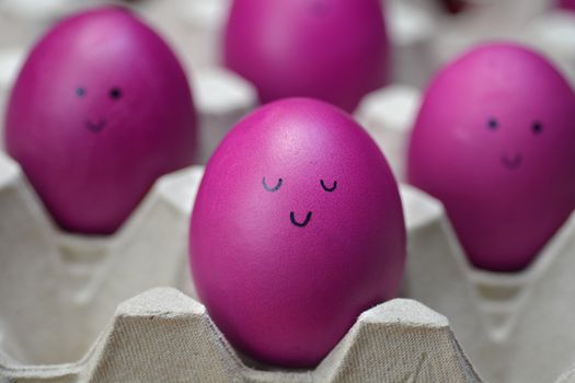 Pink Easter eggs with drawn smiling faces on carton