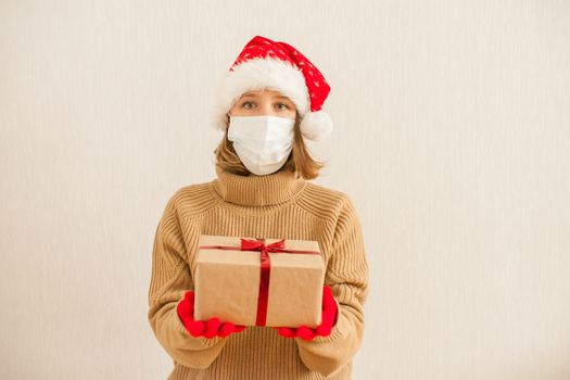 a girl in a santa hat and a medical protective mask holds gifts in her hands. New Year 2021