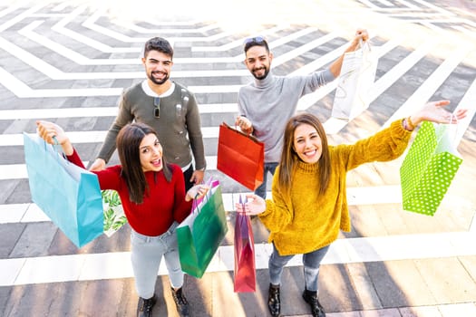 View from top of two couple outdoor in the city showing their colored shopping bags smiling and looking at the camera - Vivid colors of beautiful stylish young friends satisfied with purchases