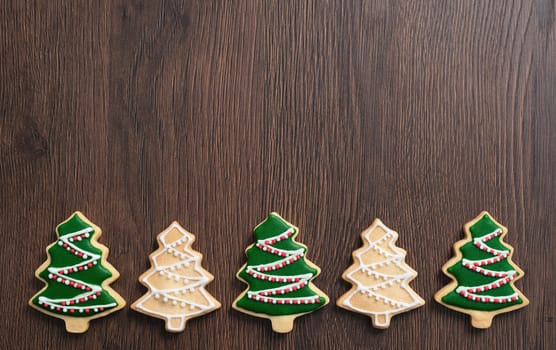 Top view of decorated Christmas tree gingerbread cookie on wooden table background with copy space, concept of holiday celebration.