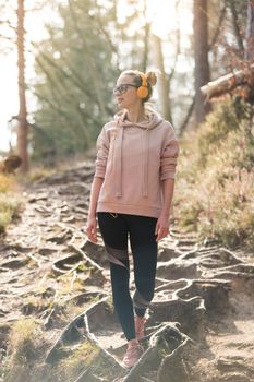 Active sporty woman listening to the music while hiking in autumn fall forest. Female jogger training outdoor. Healthy lifestyle image of young caucasian woman walking on hiking trail in nature.