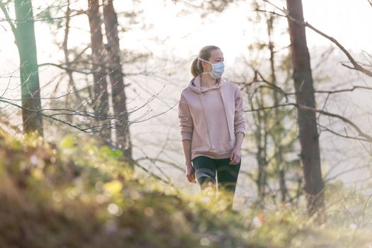 Portrait of caucasian sporty woman wearing a medical protection face mask while walking in the forest. Corona virus, or Covid-19, is spreading all over the world.