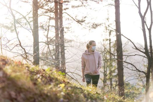 Portrait of caucasian sporty woman wearing a medical protection face mask while walking in the forest. Corona virus, or Covid-19, is spreading all over the world.