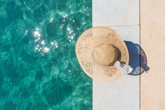 Graphic image of top down view of woman wearing big summer sun hat relaxing on pier by clear turquoise sea.