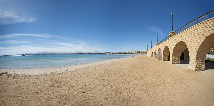 Closeup view across an empty sandy tropical beach resort shoreline with stone stone bridge walkway and arches