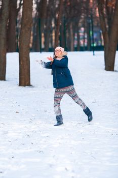 Happy teenage girl having a snowball fight, ready to throw a snowball, playing snowballs in winter park