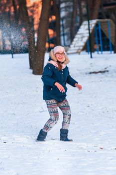 Happy teenage girl having a snowball fight, ready to throw a snowball, playing snowballs in winter park