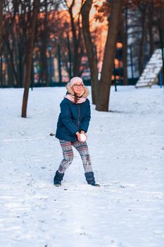 Happy teenage girl having a snowball fight, ready to throw a snowball, playing snowballs in winter park