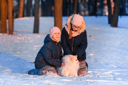Beautiful teenage girls having fun with spitz dog in the park in winter