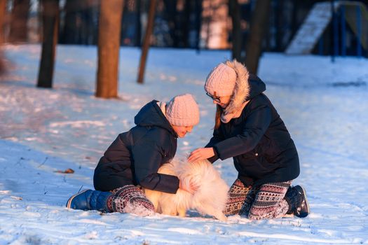 Beautiful teenage girls having fun with spitz dog in the park in winter