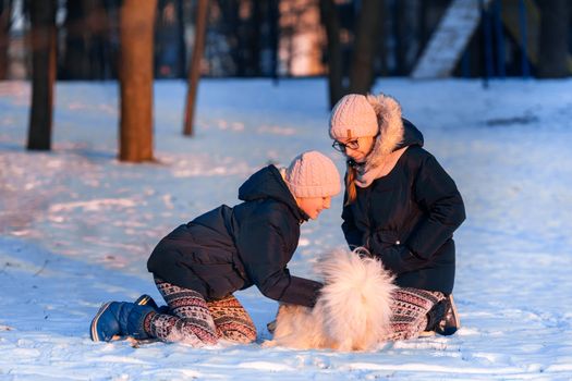 Beautiful teenage girls having fun with spitz dog in the park in winter