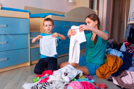 Happy children folding clothes in thier messy bedroom