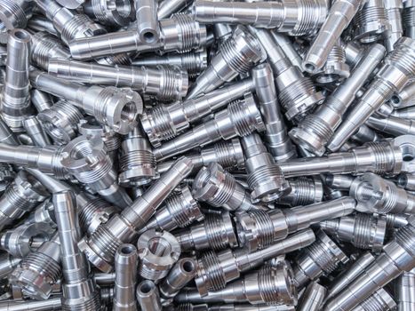 Full frame background of pile of shiny long steel parts, clean steel rods after fine cnc turning - laying chaotically with selective focus and blur.