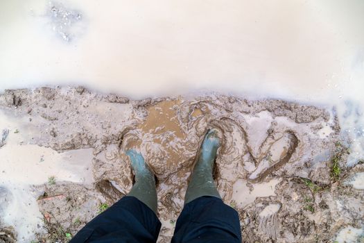 feet in green rubber boots stands in wet brown mud puddle, directly above first person gonzo view