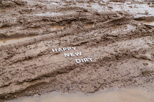 the words happy new dirt laid with silver metal letters on wet mud surface in diagonal perspective under cloudy autumn day light