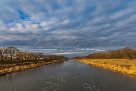 Cloudy landscape of river between yellow coasts and trees