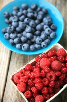 Blueberries in a blue glass bowl and raspberries in a paper box