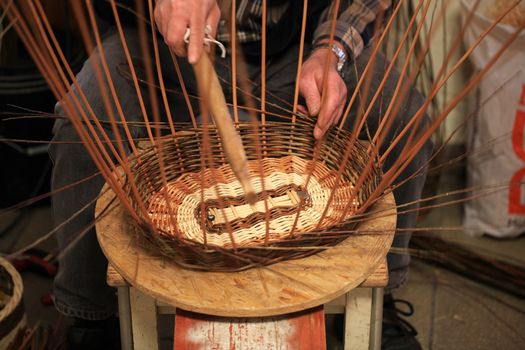 Hands of an old craftsman working on a wicker basket