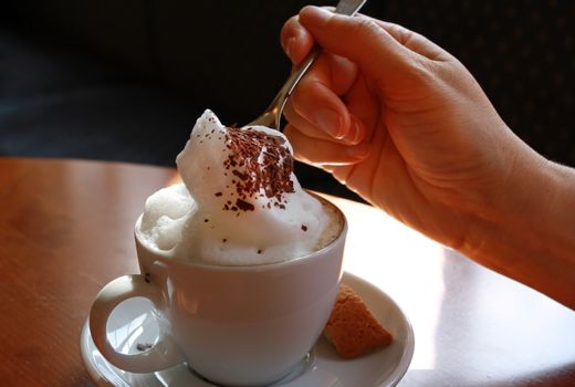 Hand with teaspoon stirring in a cup of cappuccino