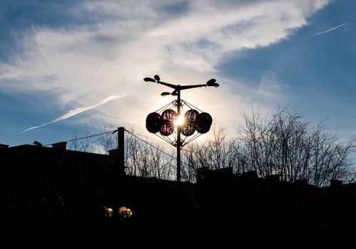 Sun shining behind christmas decoration on city lamp