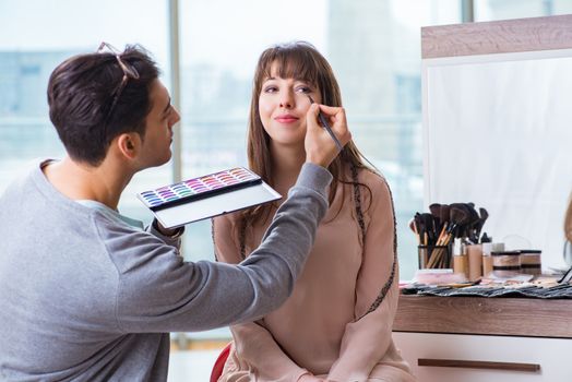 Man doing make-up for cute woman in beauty salon