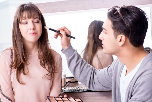 Man doing make-up for cute woman in beauty salon