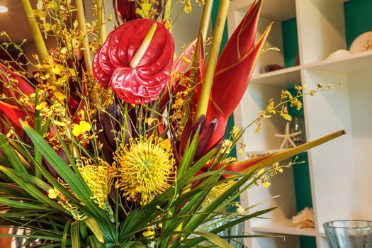 Tropical bouquet of flowers including Heliconia bihai, yellow oncidium orchids, yellow pincushion protea, and red anthuriums.