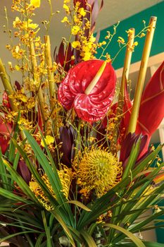 Tropical bouquet of flowers including Heliconia bihai, yellow oncidium orchids, yellow pincushion protea, and red anthuriums.