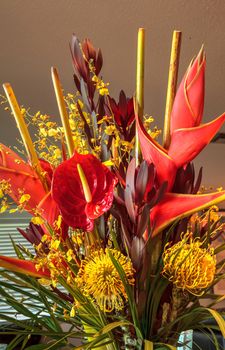 Tropical bouquet of flowers including Heliconia bihai, yellow oncidium orchids, yellow pincushion protea, and red anthuriums.