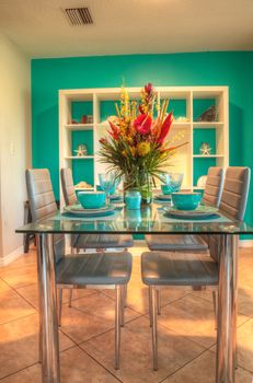 Tropical blue table set with flowers including Heliconia bihai, yellow oncidium orchids, yellow pincushion protea, and red anthuriums.